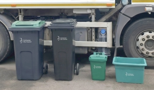 A Colchester City Council refuse lorry and several bins lined up beside it.